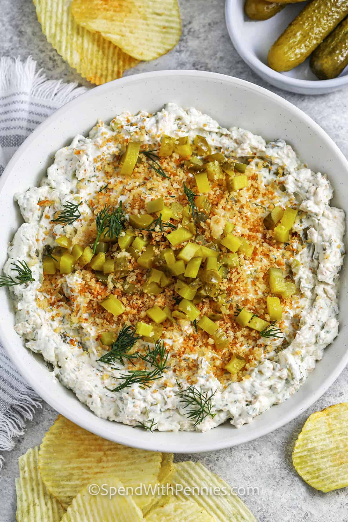 County fair deep-fried pickles are reimagined as a delicious fried pickle dip! Cream cheese and sour cream mix with diced pickles, savory spices, and crispy parmesan breadcrumbs in this tangy recipe. Try different flavors like ranch or buffalo for a twist. Made with pantry ingredients, this dip is a mouthwatering taste of the south. #spendwithpennies plated Fried Pickle Dip with chips