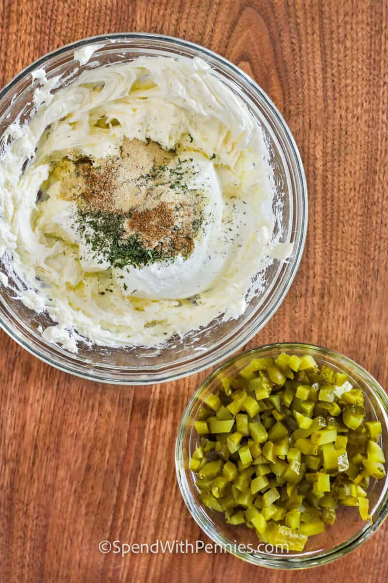 Fried pickle dip is a tangy and savory treat made with creamy ingredients and chopped pickles, perfect for satisfying snack cravings. This versatile dip can be switched up with add-ins like crispy bacon, shredded cheese, or a splash of hot sauce, making it a hit at any gathering. #spendwithpennies ingredients to make Fried Pickle Dip in a bowl and a bowl of pickles