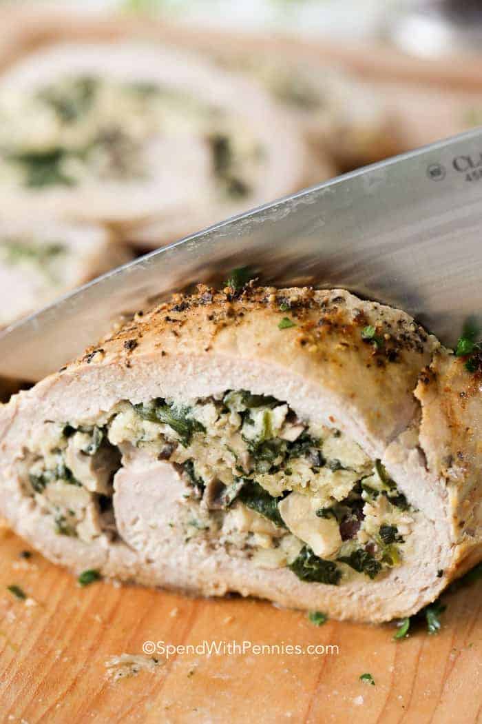 Stuffed Pork Tenderloin on a board being cut with a knife