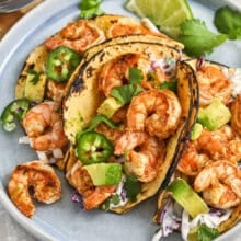 A plate of shrimp tacos topped with jalapenos, avocados, cilantro, and limes