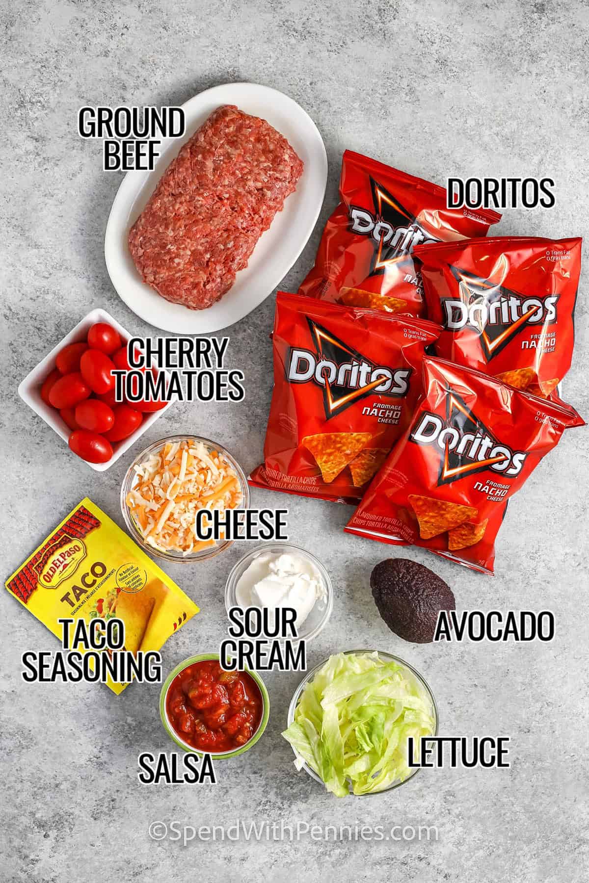 ingredients to make walking tacos labelled: ground beef, doritos, cherry tomatoes, cheese, taco seasonings, sour cream, salsa, lettuce, and avocado.