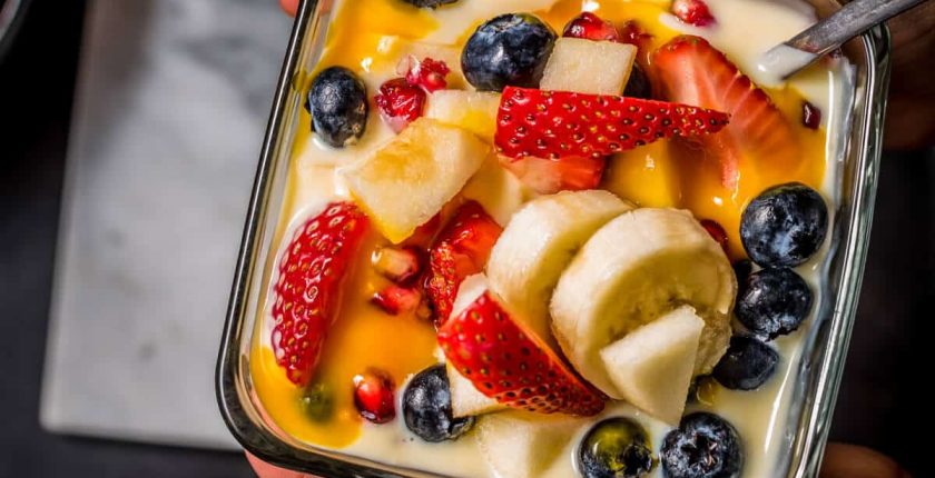 An overhead shot of a child holding a bowl of fruit custard. Another bowl is placed on a marble board.